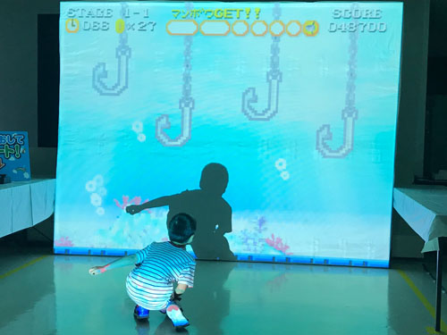 子供たちがスクリーン前で体を動かし深海魚を集めるイベント風景1